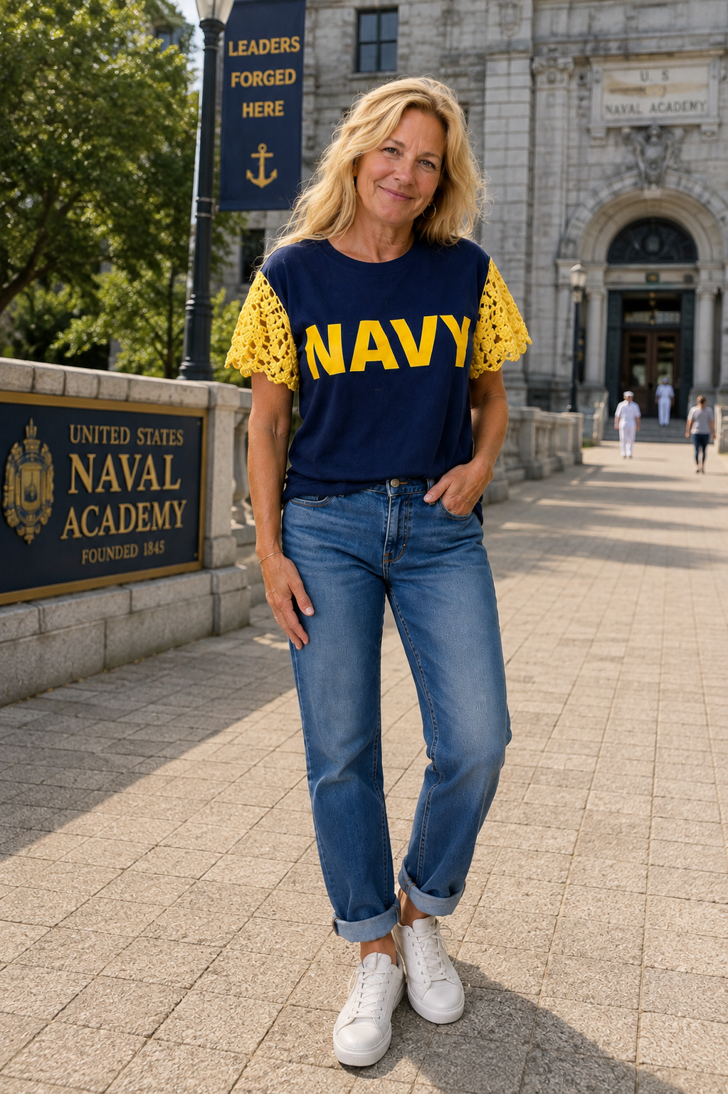 A woman wearing a navy blue NAVY graphic T-shirt reimagined with yellow hand-crocheted cap sleeves paired with blue jeans and white sneakers. 