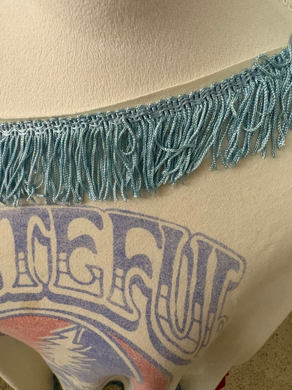 Close-up of light blue fringe trim across the neckline of tee with red and blue Grateful Dead graphic.