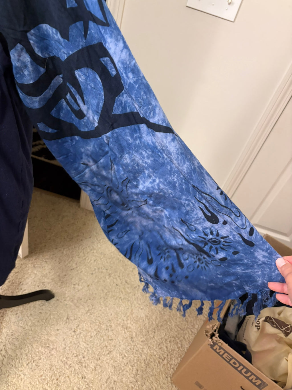 A blue and black tie-dye fringed scarf with abstract patterns made into a unique sleeve. 