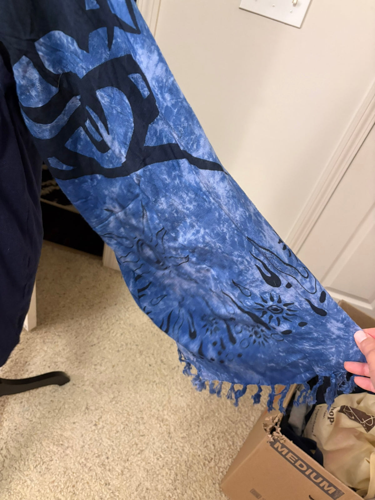 A blue and black tie-dye fringed scarf with abstract patterns made into a unique sleeve. 